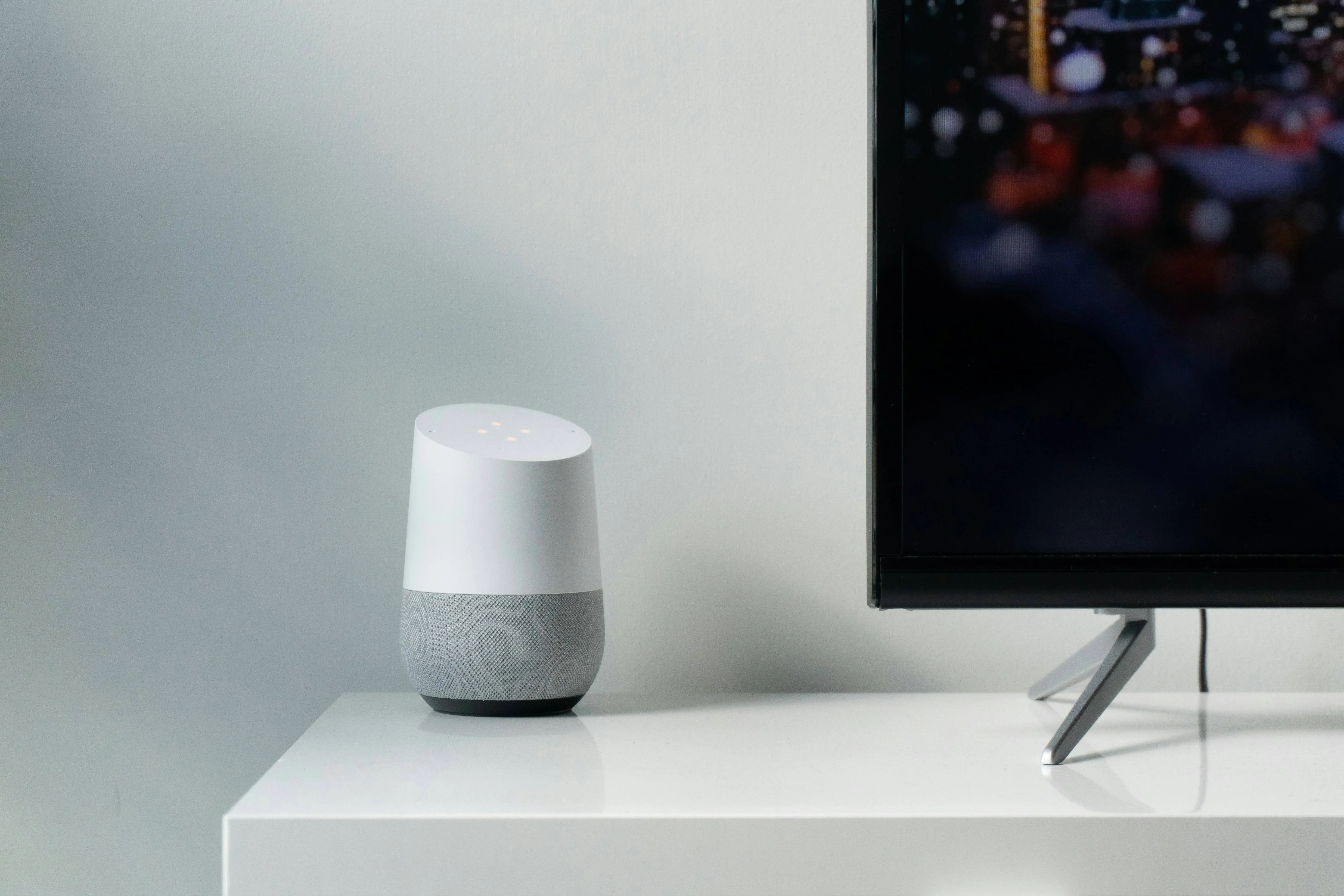 Google Home smart speaker on a white shelf beside a TV