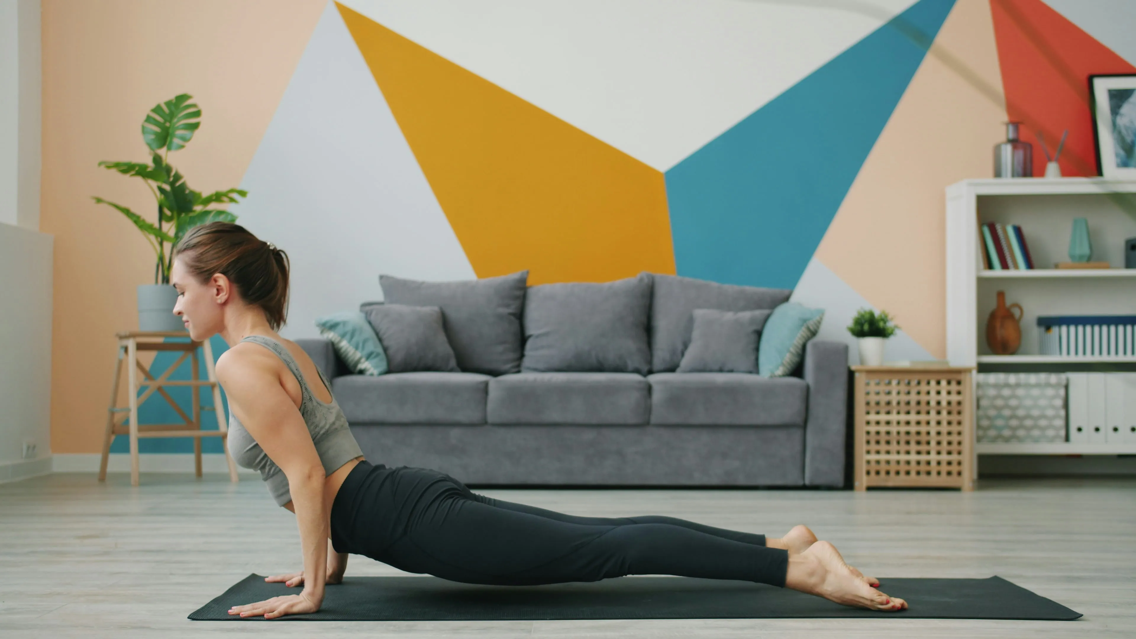 Woman doing an upward dog yoga pose on a mat in a bright living room
