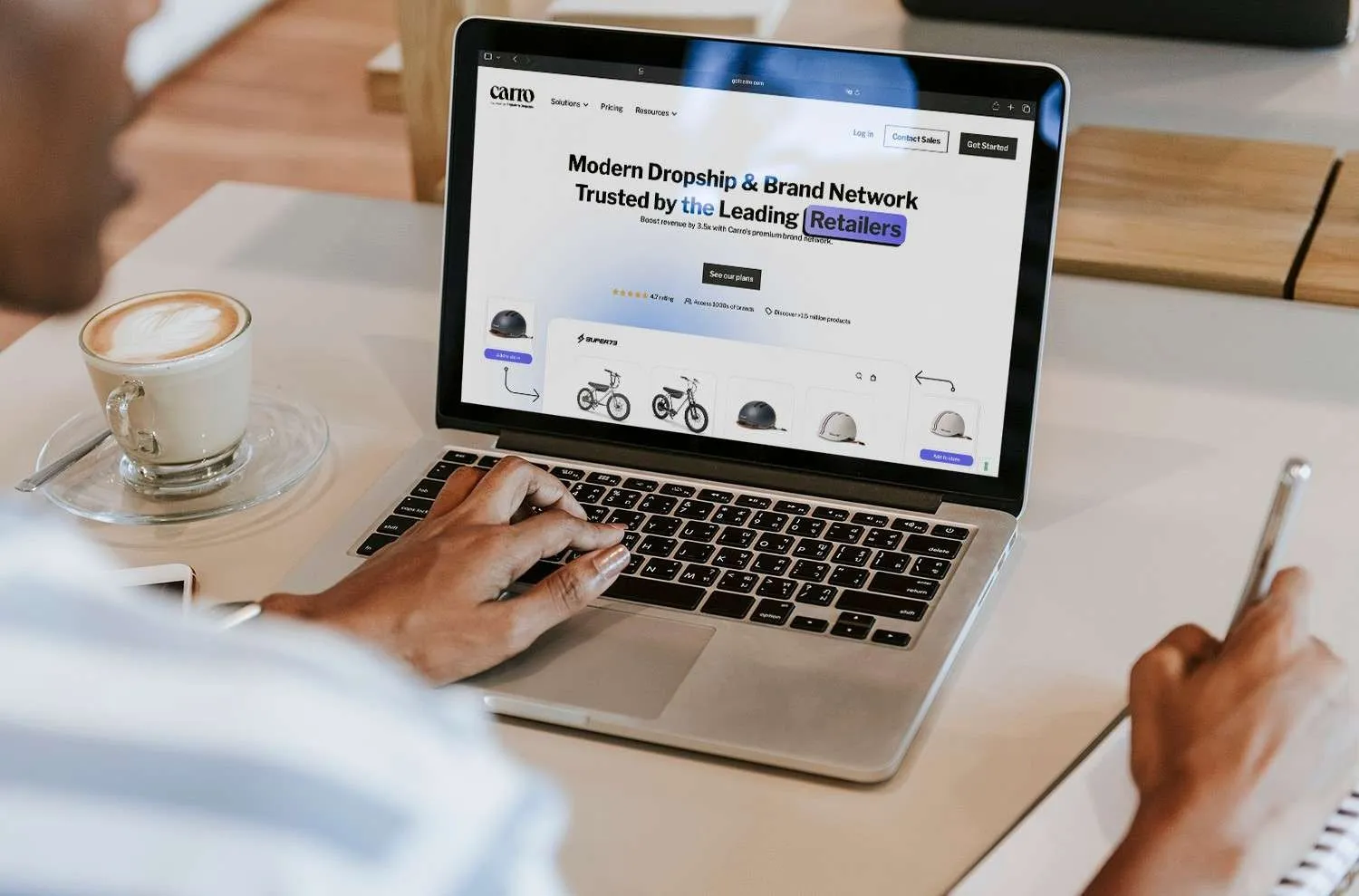 Person typing on a laptop showing the Carro homepage with Super73 bikes and helmets